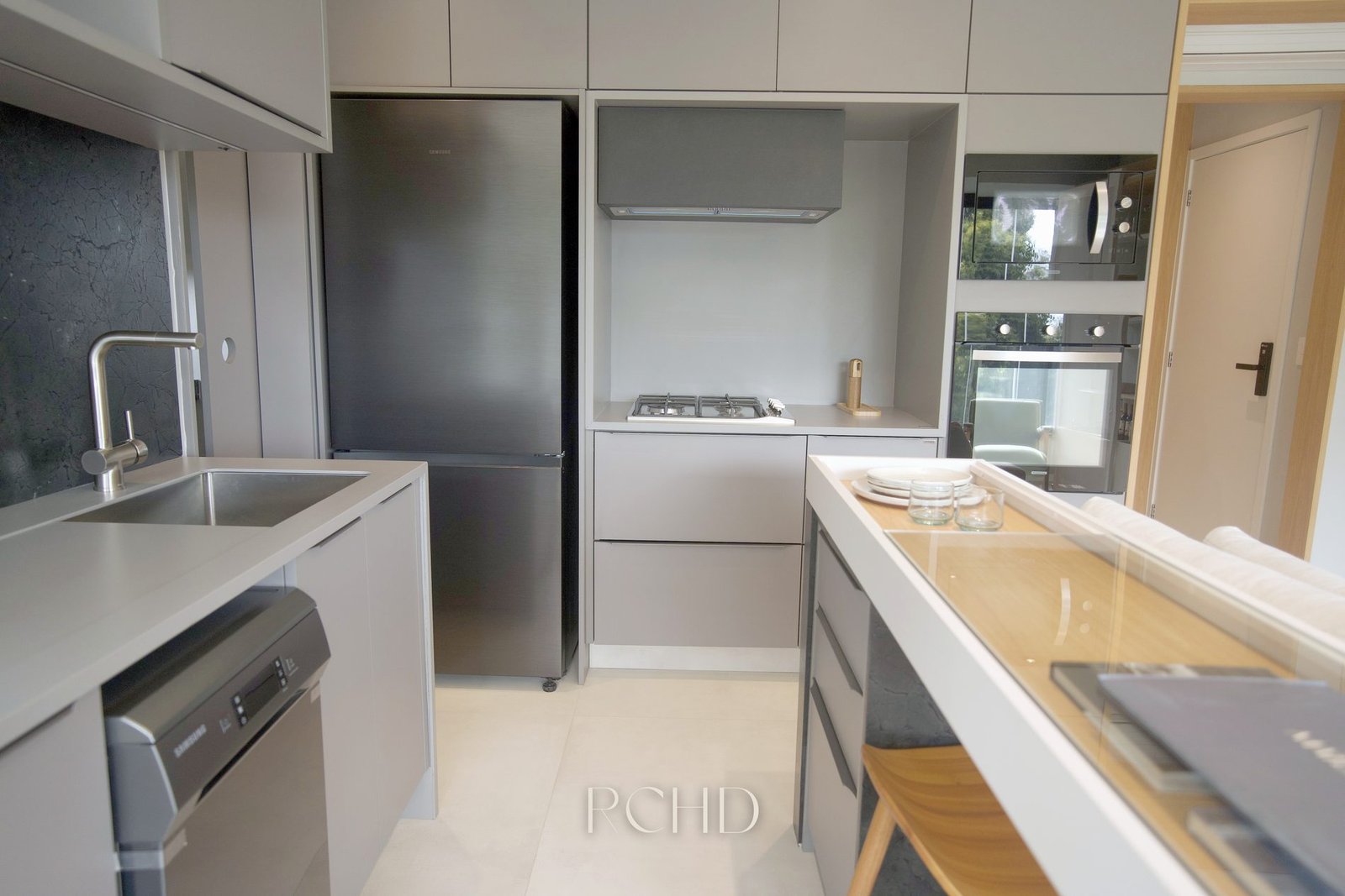 Cozinha do apartamento decorado, com bancada, torre de fornos e passagem para a área de serviço